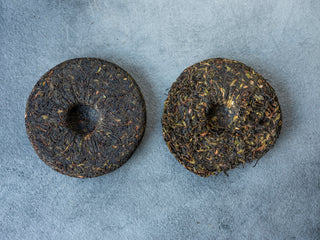 Two round, dark brown tea cakes on a gray surface